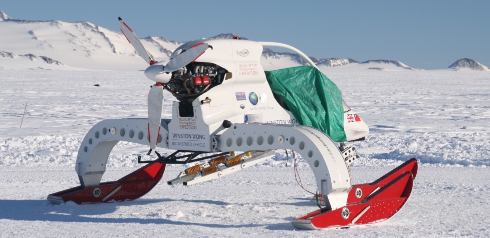 A futuristic, white snow vehicle with red skis and a visible engine—ideal for Antarctic Logistics and Expeditions—is parked on a snowy, mountainous landscape in Antarctica, partially covered with a green tarp.