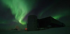 Green aurora borealis lights swirl above an industrial-looking building in the snowy, remote landscape of Antarctica. Faint stars shine through the glowing sky, highlighting the cold solitude faced by Antarctic Logistics and Expeditions teams.