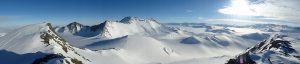Panoramic view of snow-covered mountains and valleys under a clear blue sky in Antarctica, with the sun shining brightly and casting light over the vast, icy landscape—an awe-inspiring scene from Antarctic Logistics and Expeditions.