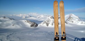 A pair of wooden skis stands upright in snow, overlooking a vast Antarctic landscape under a clear blue sky—jagged peaks and snow-covered valleys evoke the spirit of adventure with Antarctic Logistics and Expeditions.