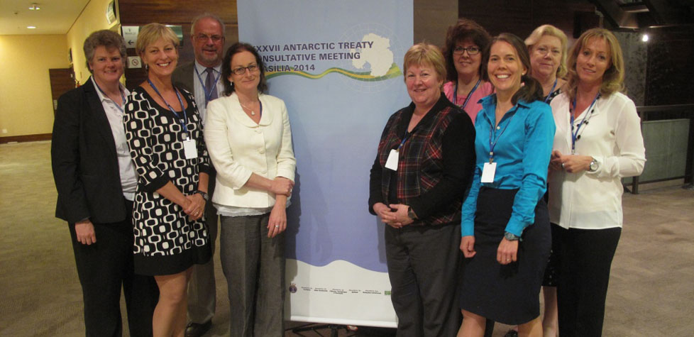 Ten people, wearing conference badges, stand smiling in front of a banner for the XXXVII Antarctic Treaty Consultative Meeting (Brasilia, 2014), indoors and dressed in business casual and formal attire, highlighting their commitment to Antarctica's future and effective Antarctic logistics.