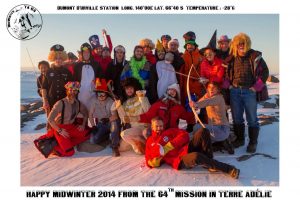 A group of people in colorful costumes pose together on a snowy landscape at sunset, celebrating Midwinter 2014 at Dumont D’Urville Station in Antarctica, showcasing the spirit of the South Pole and Antarctic Logistics and Expeditions.