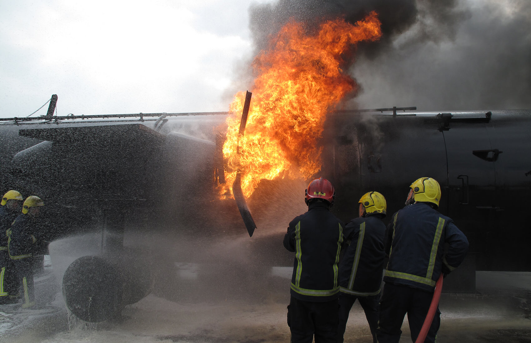 Firefighters in protective gear spray water on a large black aircraft engulfed in flames and heavy smoke, working to extinguish the fire near the plane's fuselage during an Antarctic Logistics and Expeditions operation.