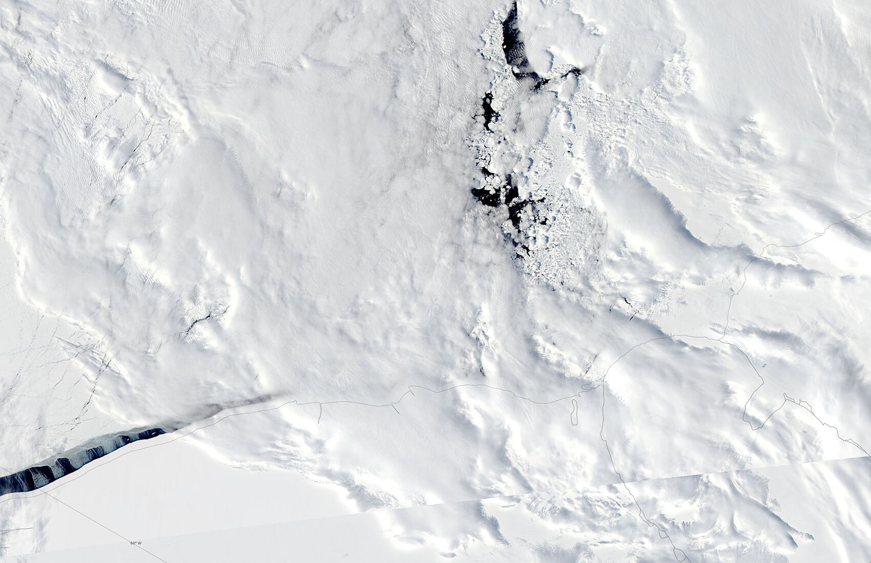 A satellite view of Antarctica's vast icy landscape reveals cracks, textured snow, and dark patches of exposed water or ice near the center, capturing the rugged, frozen environment of the South Pole.
