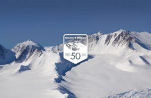 Snow-covered mountain peaks under a clear blue sky in Antarctica, with a graphic in the center reading Mount Vinson 50, 1966-2016 to commemorate the 50th anniversary of the mountain’s first ascent near the South Pole.