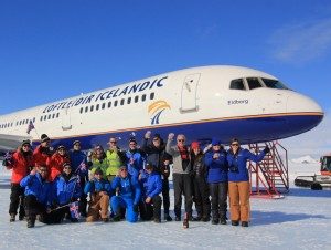 A group of people in winter clothing pose together in front of an Icelandair airplane on a snowy surface under a clear blue sky, capturing the spirit of Antarctic Logistics and Expeditions.