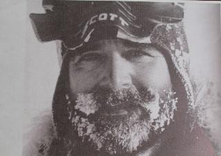 A man wearing snow goggles and a winter hat is shown in close-up with snow and ice covering his beard and mustache, capturing the harsh conditions faced during Antarctic Logistics and Expeditions in Antarctica.
