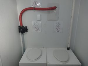 Two toilet seats sit side by side in a small restroom, typical of remote Antarctica outposts. Above them, signs show permitted and forbidden toilet positions. A red pipe runs along the wall—a glimpse into South Pole life with Antarctic Logistics and Expeditions.