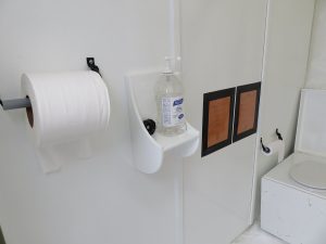 A white restroom at the South Pole features a large toilet paper roll, wall-mounted hand sanitizer, two plaques, and a toilet with a smaller roll—reflecting the practicality essential for Antarctic Logistics and Expeditions in Antarctica.