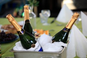 Three bottles of sparkling wine chilled in ice in a metal container on a table set for a celebration, evoking the adventurous spirit of Antarctic Logistics and Expeditions, with glassware and plates of food ready to toast the wonders of Antarctica.