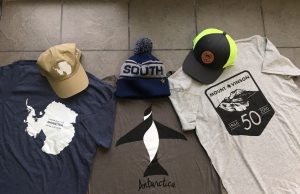 Three hats and three T-shirts with Antarctic themes are displayed on a stone floor. Designs include a map of Antarctica, a penguin, Mount Vinson graphics, and one hat reading SOUTH—perfect for South Pole or Antarctic Logistics and Expeditions fans.
