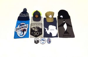 Five caps and three t-shirts with Antarctica-themed designs are arranged in a row, with three round patches featuring South Pole imagery placed below the t-shirts, all on a white background.