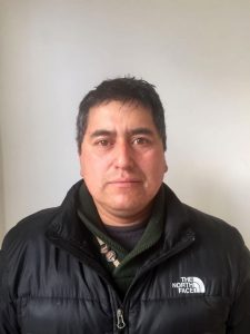 A man with short dark hair wears a dark North Face jacket and a green sweater, standing against a plain white background, looking directly at the camera with a neutral expression—ready for Antarctic Logistics and Expeditions in Antarctica.