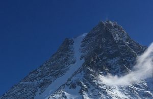 Snow-covered, rocky mountain peak rises sharply against a clear, deep blue sky in Antarctica, with a small cloud drifting at the lower right—an awe-inspiring scene reminiscent of Antarctic Logistics and Expeditions near the South Pole.