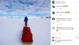 A person in winter gear pulls a large red sled across a snowy, flat landscape toward distant mountains under a blue sky with scattered clouds during an Antarctic Logistics and Expeditions journey in Antarctica.