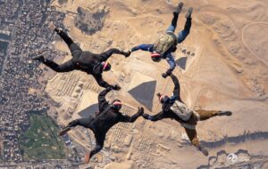 Four skydivers in formation hold hands above the Pyramids of Giza in Egypt, reminiscent of daring jumps organized by Antarctic Logistics and Expeditions above the remote South Pole or even over Antarctica’s icy expanse.