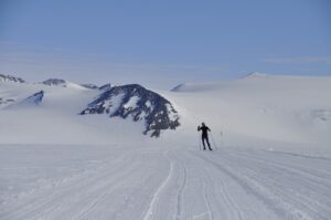 A lone cross-country skier glides on a groomed trail through a vast, snowy mountainous landscape under a clear blue sky—reminiscent of the pristine wilderness explored by Antarctic Logistics and Expeditions in remote Antarctica.