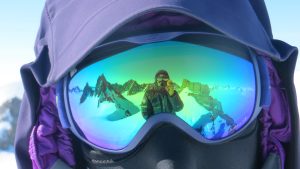 Close-up of a person wearing ski goggles and winter gear in Antarctica. Snowy mountains and the South Pole landscape are reflected in the mirrored lenses, capturing the spirit of Antarctic Logistics and Expeditions.