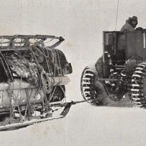 A person drives a tracked snow vehicle towing a heavy sled loaded with supplies, all moving through a snowy, icy landscape. The scene appears cold and remote.