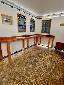 A small room with wooden counters along two walls, large informational posters about an overnight trip at the South Pole, a framed photo, a red folding chair, and a window letting in natural light.